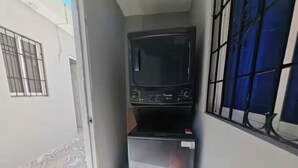 Ein schmales Zimmer mit Fernseher, kleinem Kühlschrank und einem Fenster mit Gitterstäben.