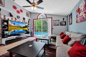 Ein Wohnzimmer mit Fernseher, Sofa, Couchtisch und Blick auf einen Pool.