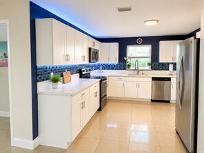 Eine moderne Küche mit weißen Schränken, einem Edelstahlkühlschrank und einer blauen Fliesenrückwand.