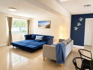 Ein Wohnzimmer mit einem blauen Sofa, einem grauen Sofa, einem Glastisch und einer Lampe.