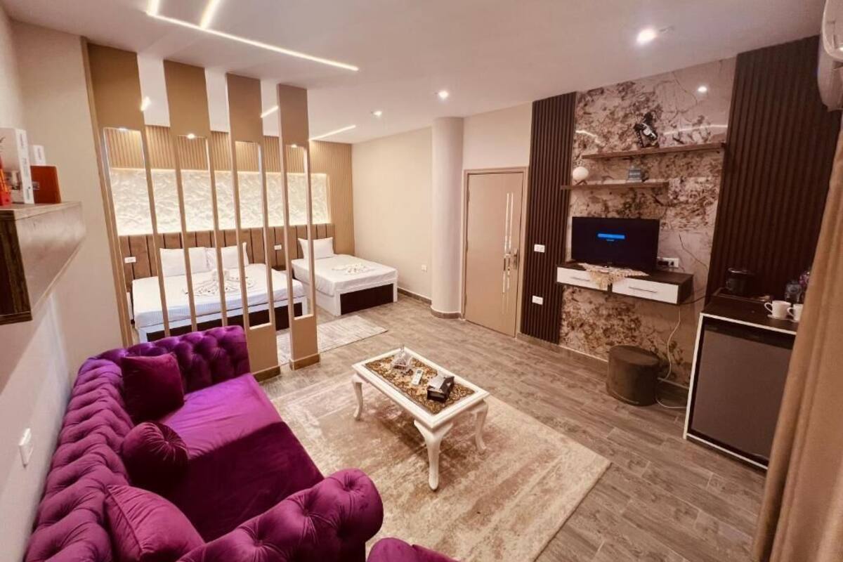 A modern living room with a sofa, a coffee table, a TV, and a kitchen area.