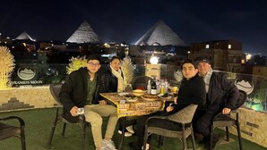 A group of people dining at a table with a view of pyramids in the background. - pyramids Moon IIn (Giza)