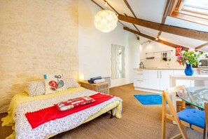 A bedroom with a bed, a desk, and a kitchenette in the background. - "Le Petit Studio" Apartment with Shared Garden and Wi-Fi (Riec-sur-Bélon)