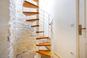 Un escalier en colimaçon avec des marches en bois et une rampe blanche, menant à une porte dotée d’une poignée en laiton.