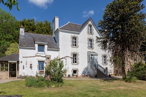 A two-story house with a stone facade, a visible staircase, and a garden with potted plants. - "Le Petit Studio" Apartment with Shared Garden and Wi-Fi (Riec-sur-Bélon)
