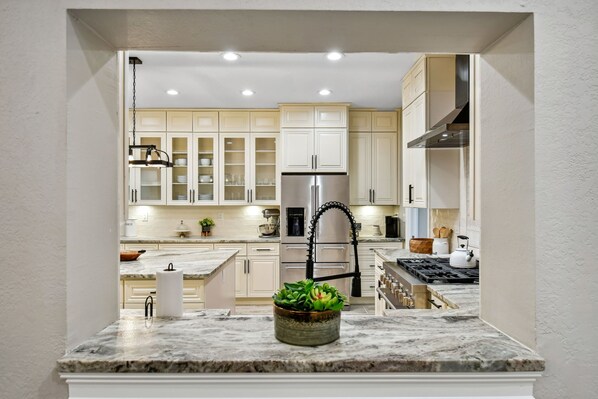 A kitchen with white cabinets, a stainless steel refrigerator, a gas stove, and a marble countertop.