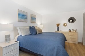 Ein Schlafzimmer mit Bett, Nachttischen, einer Kommode, Wandbildern und einem dekorativen Wandelement.