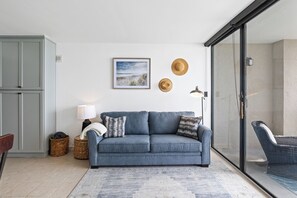 Ein Wohnzimmer mit einer Couch, einer Lampe, einem Bilderrahmen und einem Korbstuhl.