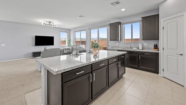 A modern kitchen with dark cabinetry, a large island, and a flat-screen TV mounted on the wall. - The Great Las Vegas Escape 4 bed 2.5 bath (Las Vegas)