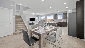 A modern kitchen with dark cabinets, a dining area with a table set for four, and a staircase leading to another level. - The Great Las Vegas Escape 4 bed 2.5 bath (Las Vegas)