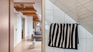 Ein Flur mit Holzboden, einer Glastrennwand und Blick in einen Wohnbereich mit Sofa und Couchtisch.