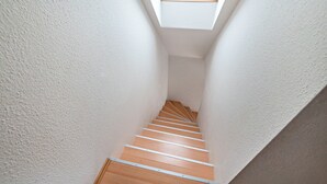Eine enge Treppe mit Holzstufen und weißen Wänden, die zu einem Oberlicht führt.