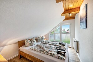 A bedroom with a sloped ceiling, a large window, a bed with striped bedding, and a radiator. - Apartment for 6 Guests (70 m²) with Shared Terrace, Garden, and Wi-Fi (Kalkhorst)