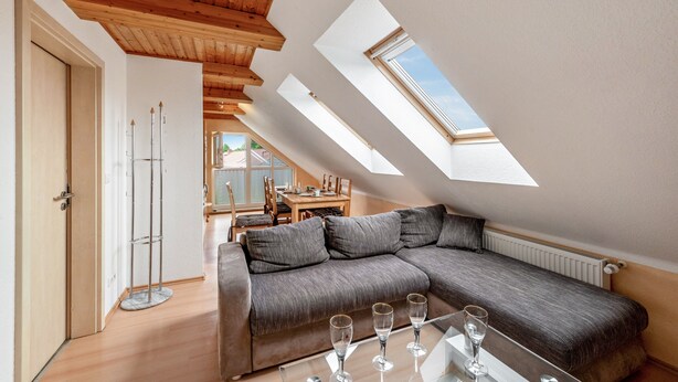 Ein Loft-Zimmer mit Ecksofa, Dachfenstern, einer Essecke und einem Glastisch mit Gläsern.