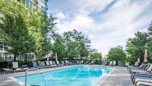 Ein rechteckiger Pool mit Metallleiter, umgeben von Liegestühlen und Bäumen, mit blauem Himmel darüber.