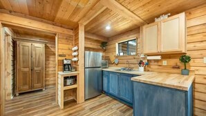 L’intérieur d’une cabane en bois comprend un espace cuisine équipé de placards, d’un réfrigérateur et d’un évier.