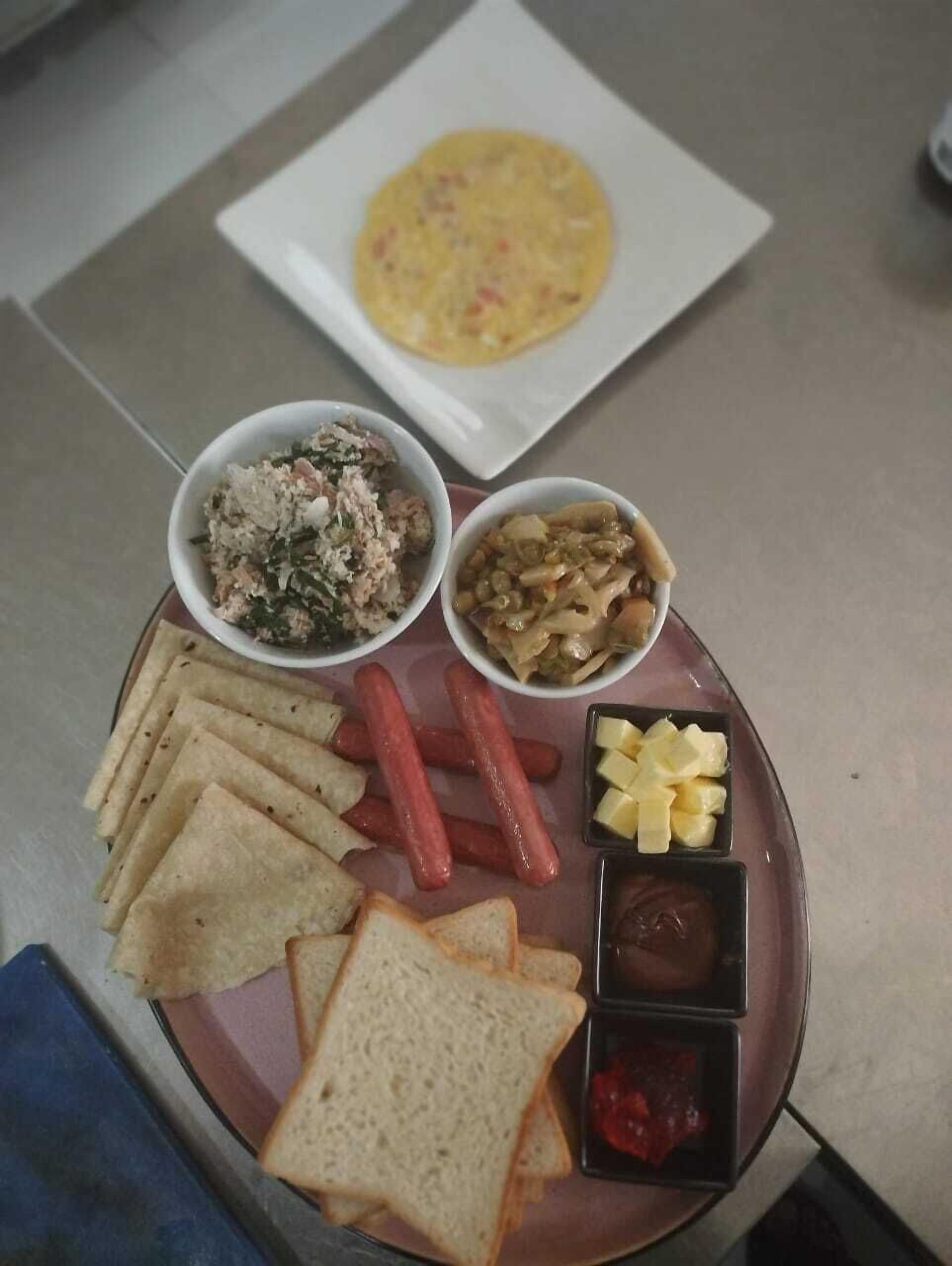 A meal tray with various food items including a plate of hot dogs, cheese, and condiments, along with two bowls of side dishes.