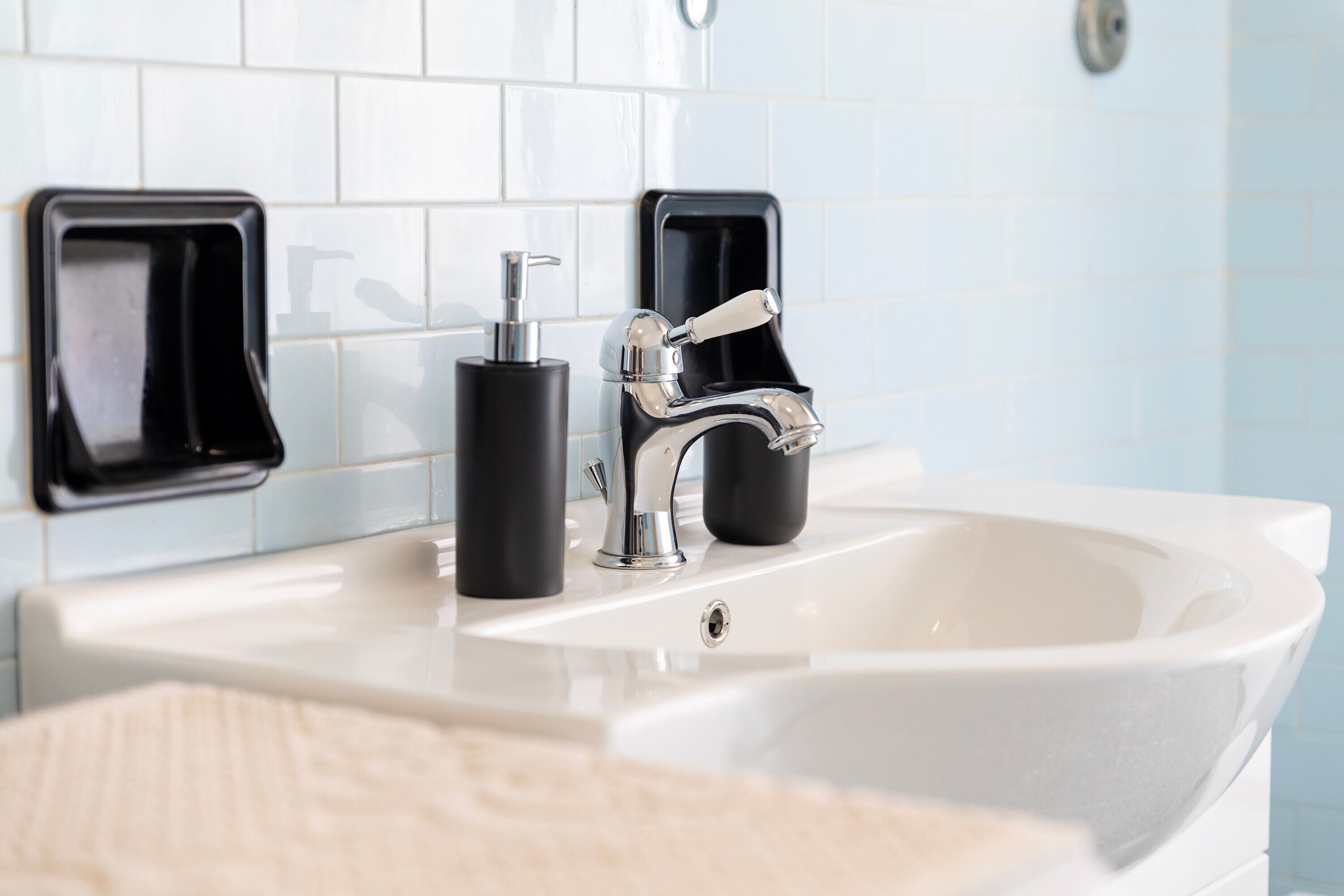 Une salle de bain avec un lavabo blanc, un robinet chromé et deux distributeurs de savon noirs.