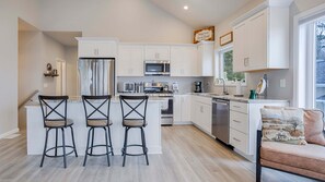 A modern kitchen with white cabinets, a central island with bar stools, a microwave, stove, and dishwasher. - Coach-ella on the Lake - Ideal Canandaigua Lake Couples Retreat! (Canandaigua)