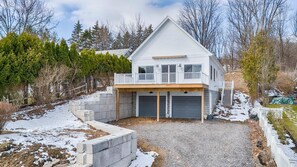 A two-story house with a covered patio, a garage, and a stone retaining wall. - Coach-ella on the Lake - Ideal Canandaigua Lake Couples Retreat! (Canandaigua)