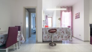 Ein Essbereich mit Tisch, Stühlen und einem Barhocker. Ein Fenster mit Vorhängen und ein Bild an der Wand.