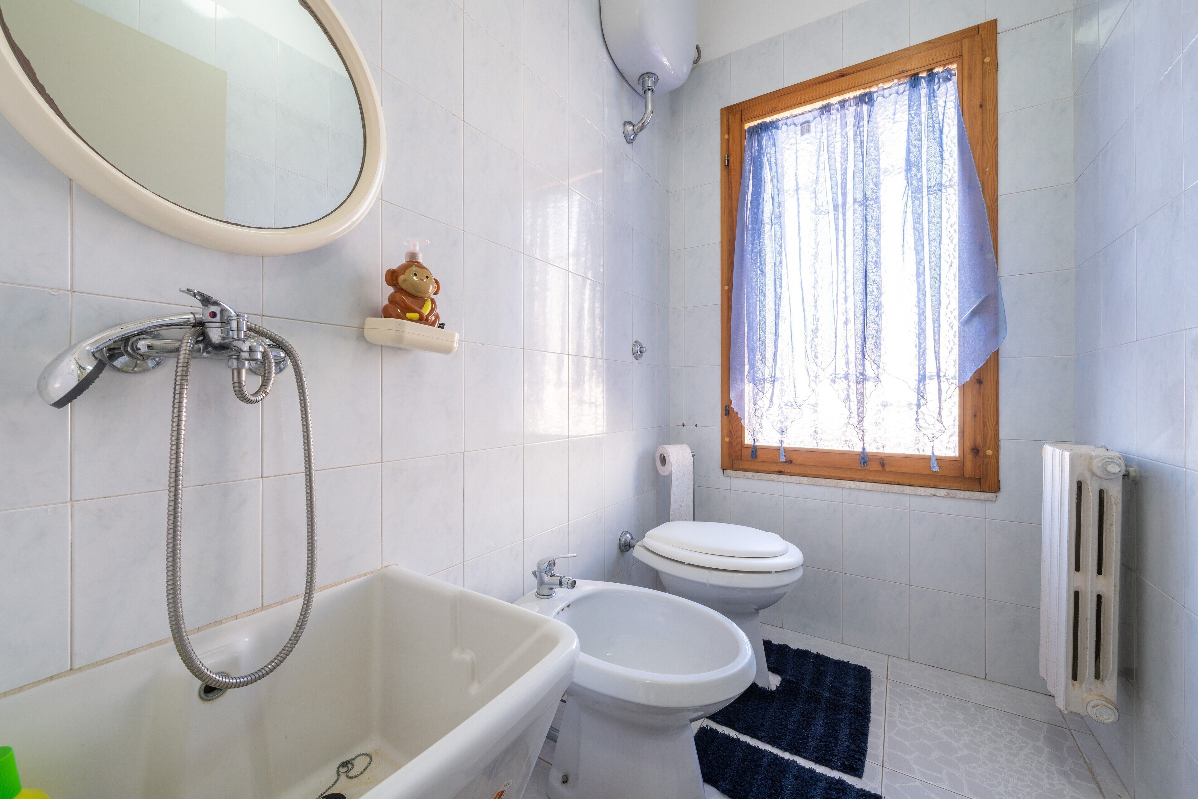 Een badkamer met een bad, een wastafel, een toilet en een raam met gordijn.