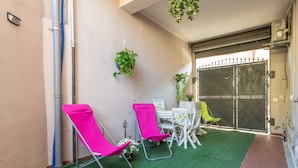 Ein kleiner Patio-Bereich mit zwei rosafarbenen Stühlen, einem Tisch mit weißem Tischlein und hängenden Pflanzen.
