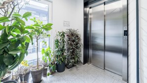 An elevator with a metallic finish, surrounded by potted plants, and a window with a view of buildings. - Wilczak 16A Cosy Studio (Poznań)
