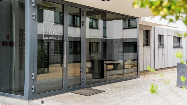 A modern building entrance with glass doors, a visible logo, and a bench outside. - Wilczak 16A Cosy Studio (Poznań)
