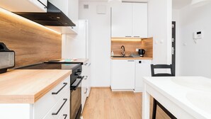 A compact kitchen with white cabinets, a wooden countertop, a black range hood, and a small dining area with a white table. - Wilczak 16A Cosy Studio (Poznań)