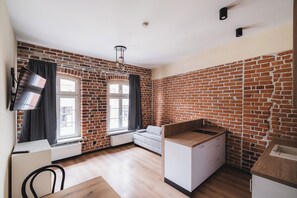 Ein Zimmer mit Backsteinwänden, einem weißen Sofa, einer kleinen Küchenzeile und einem Fenster mit Vorhängen.