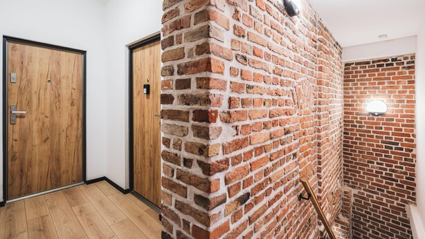 A hallway with a brick wall, wooden door, and a light fixture. - Apartament Ceglane Studio (Toruń)