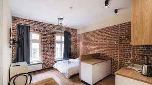 A room with a brick wall, a bed, a desk, and a window. - Apartament Ceglane Studio (Toruń)