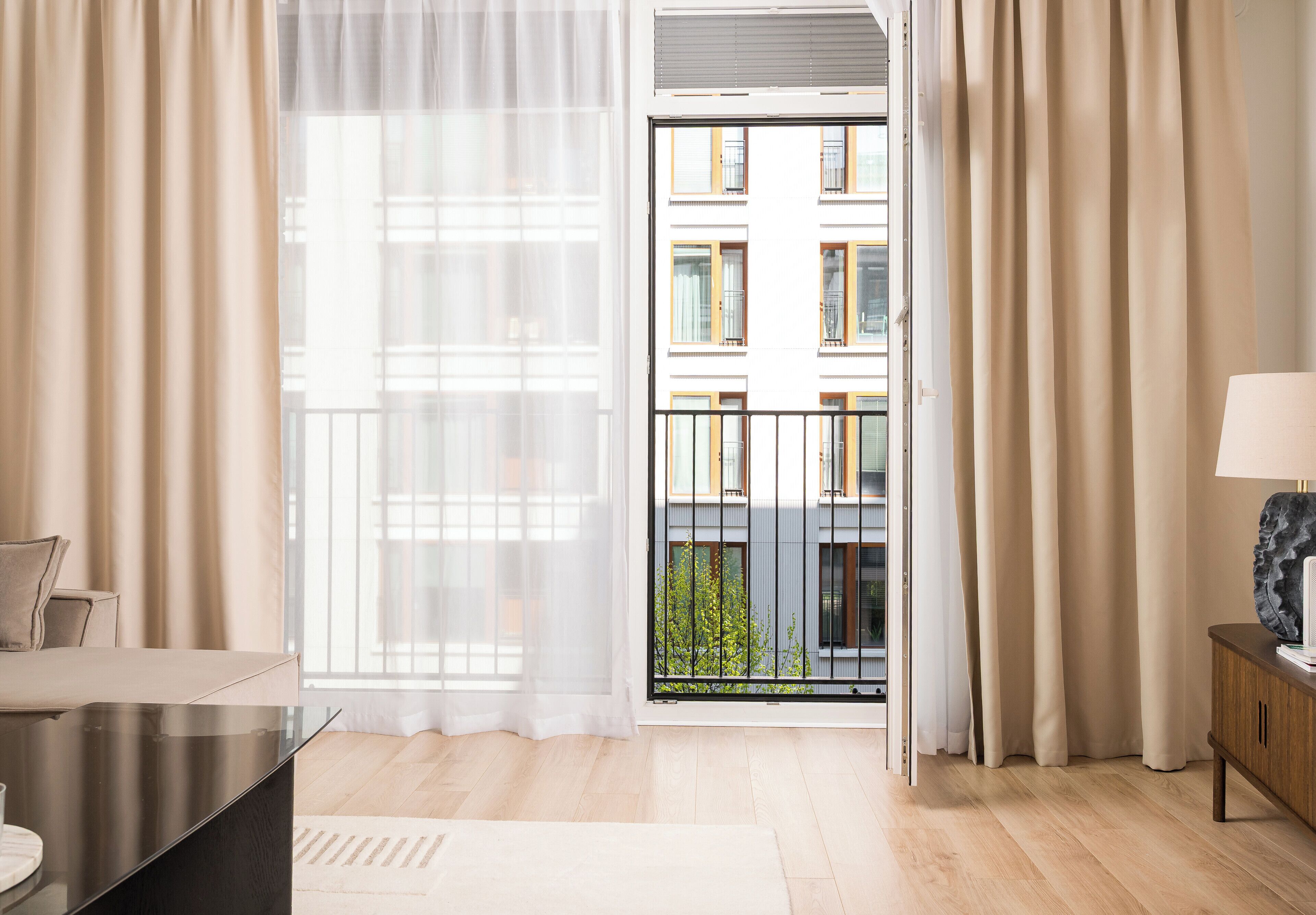 A modern living room with a sofa, a coffee table, a lamp, and a view of a balcony with a railing.