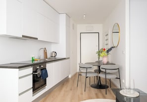 A modern kitchen with white cabinets, a black countertop, and a small dining area with a table and chairs. - Browary Warszawskie Deluxe Studio (Warszawa)