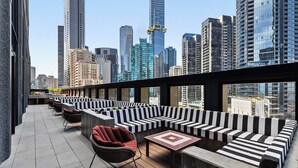 Terraço no telhado com assentos em listras preta e branca, uma cadeira de vime e uma mesa azulejada.