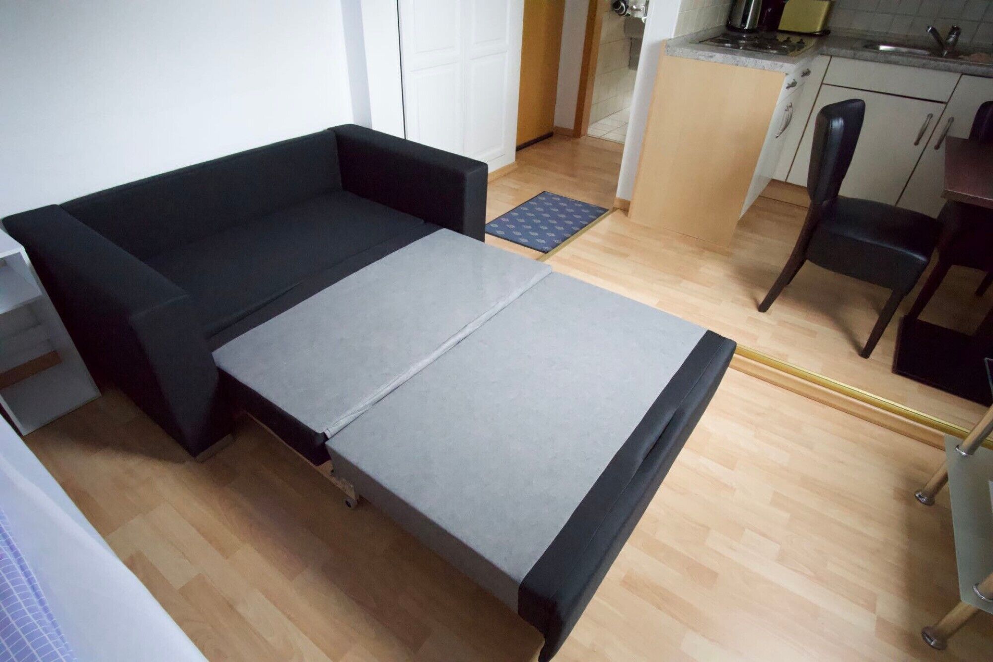 A compact room with a sofa, a pull-out bed, a small kitchen area, and a chair.