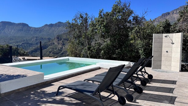 Ein Pool mit Liegestühlen, einer Steinmauer und Blick auf die Berge.