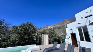 Ein Poolbereich mit Liegestühlen, einer gefliesten Wand und Blick auf das Gebirge.