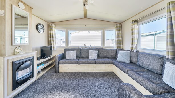 L'intérieur d'une caravane, avec un canapé, un téléviseur, une horloge et des fenêtres.