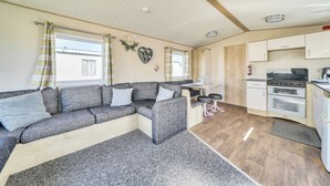 Un espace de vie compact comprenant un canapé, une petite table, un coin cuisine avec une cuisinière et un four, et une fenêtre avec des rideaux.