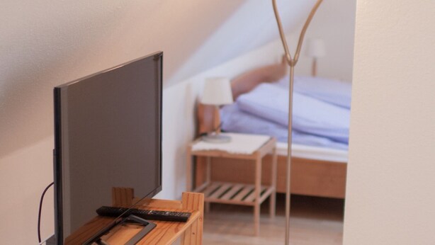 Ein Schlafzimmer mit Bett, Nachttisch, Lampe und Fernseher auf einem Holzständer.