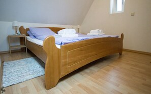 A single wooden bed in a room with a small bedside table, a lamp, and a window.