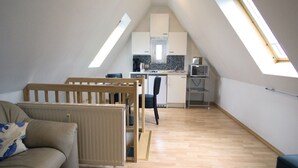 Ein Loft-Zimmer mit Küchenzeile, einem Holzstuhl, einer Couch und einem Oberlicht.