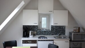 Eine kleine Küche mit weißen Schränken, einer schwarzen Küchenrückwand, einem Fenster und einer Mikrowelle.