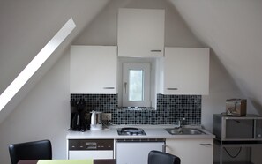 A small kitchen with white cabinets, a black tiled backsplash, a window, and a microwave.