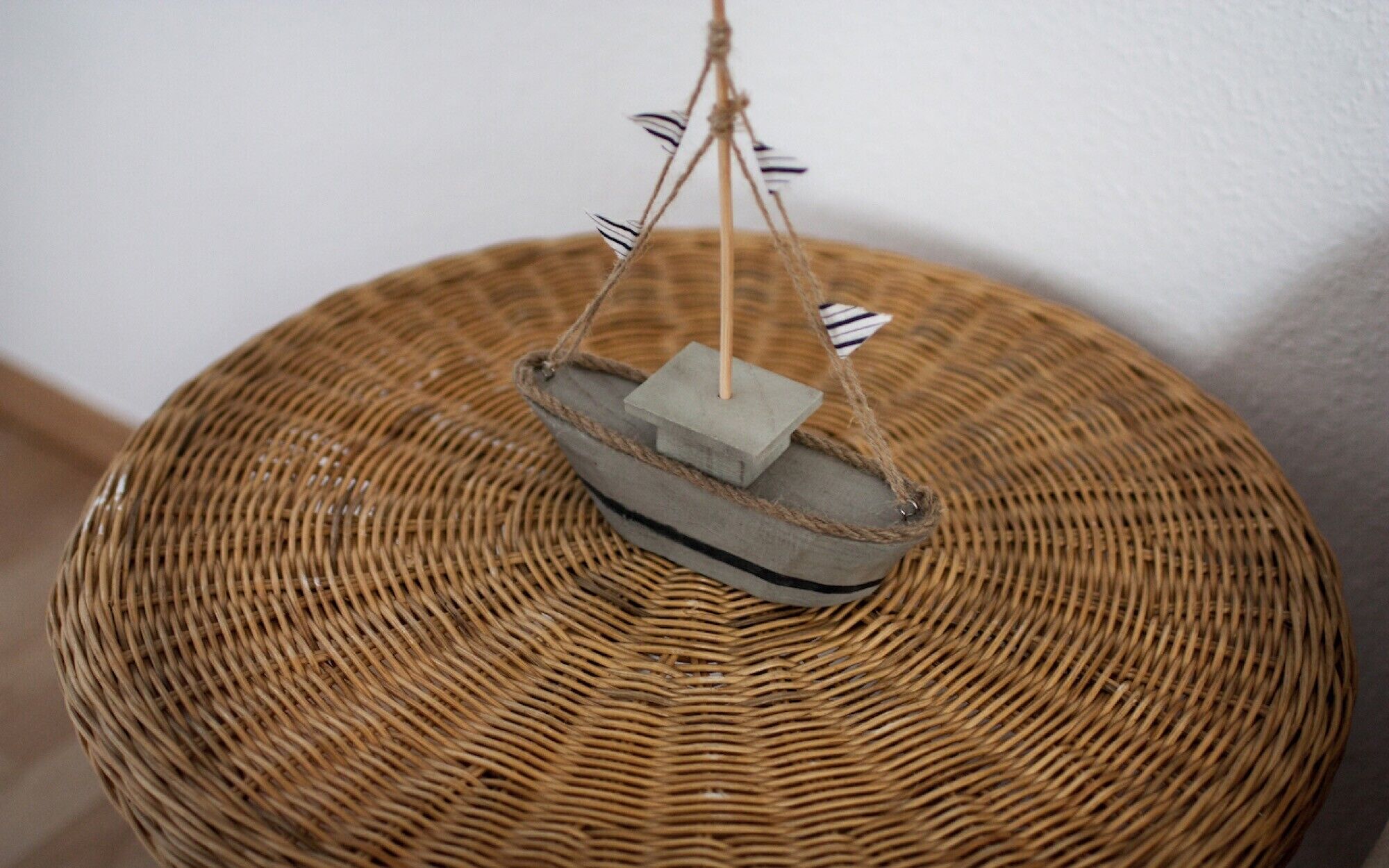 Ein kleiner, runder Tisch aus Korbmöbeln mit einem an einer Schnur hängenden Modellschiff.