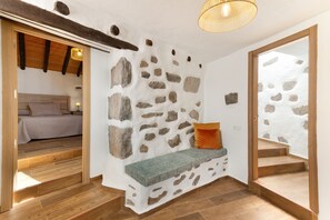 Een kamer met een stenen muur, houten vloer, een bank met kussens en een bed op de achtergrond.
