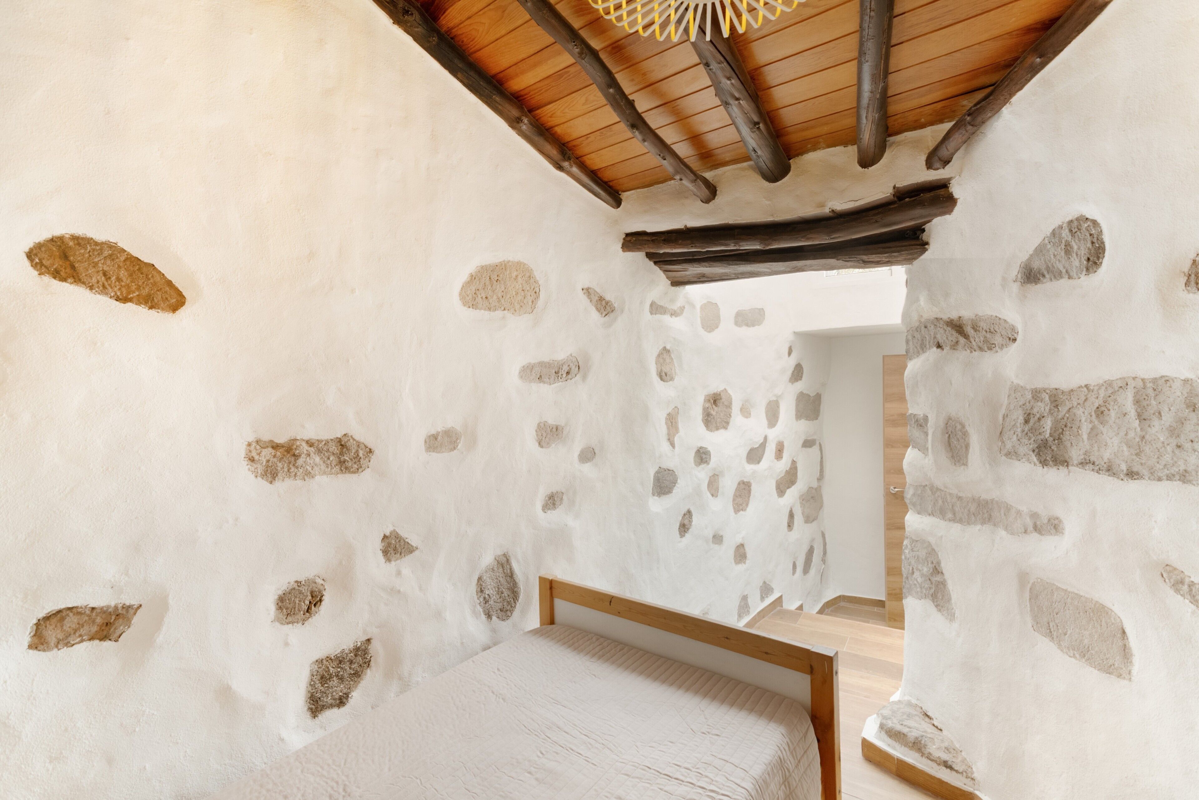 Une pièce avec un mur en pierre, un plafond en bois et un lit.