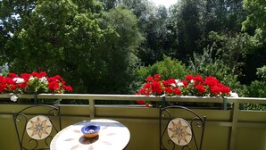 Een balkon met een tafel en stoelen, omgeven door weelderige begroeiing en rode bloemen.
